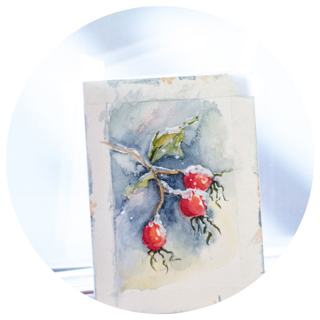 A photo of a handmade painted Christmas card with a wintry scene of a tree branch with snow covered red berries.