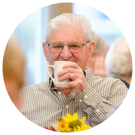 Elderly smiling man looking into the camera drinking a cup of coffee